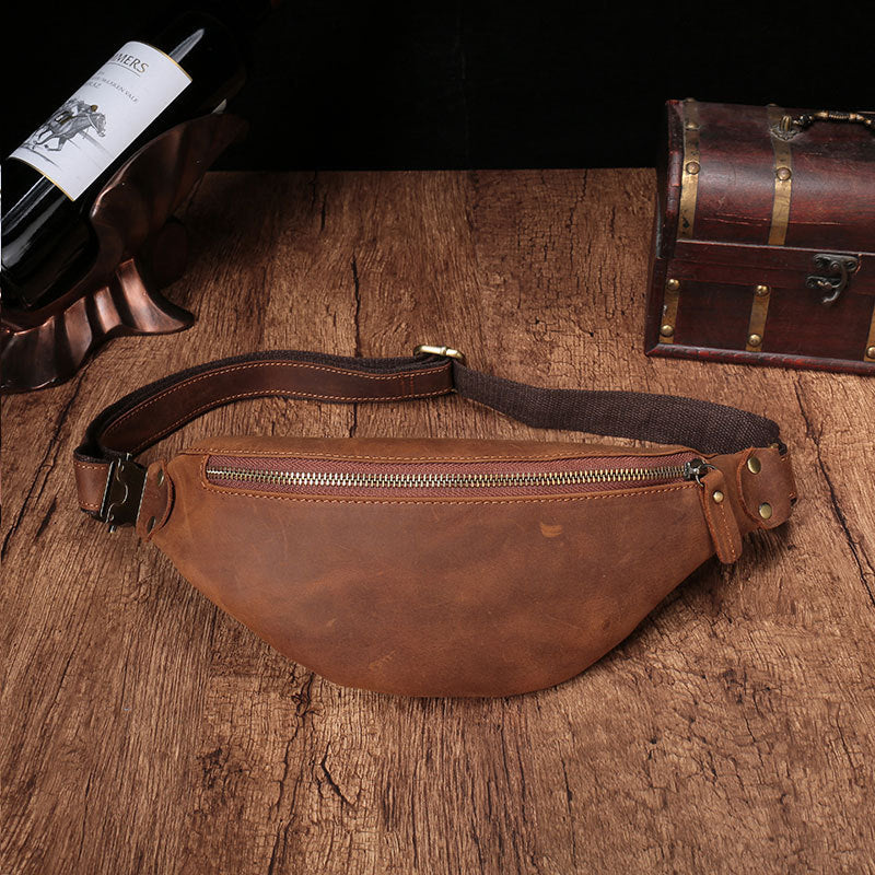 Rugged leather men's cell phone belt bag on a wooden surface with a wine bottle and vintage suitcase in the background, showcasing a functional and stylish accessory designed for modern convenience.