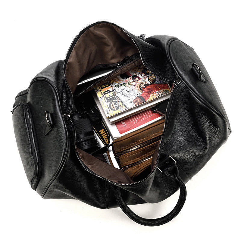 Large black leather business and travel bag with multiple compartments and zippers, showing the interior contents including books, magazines, and other items.