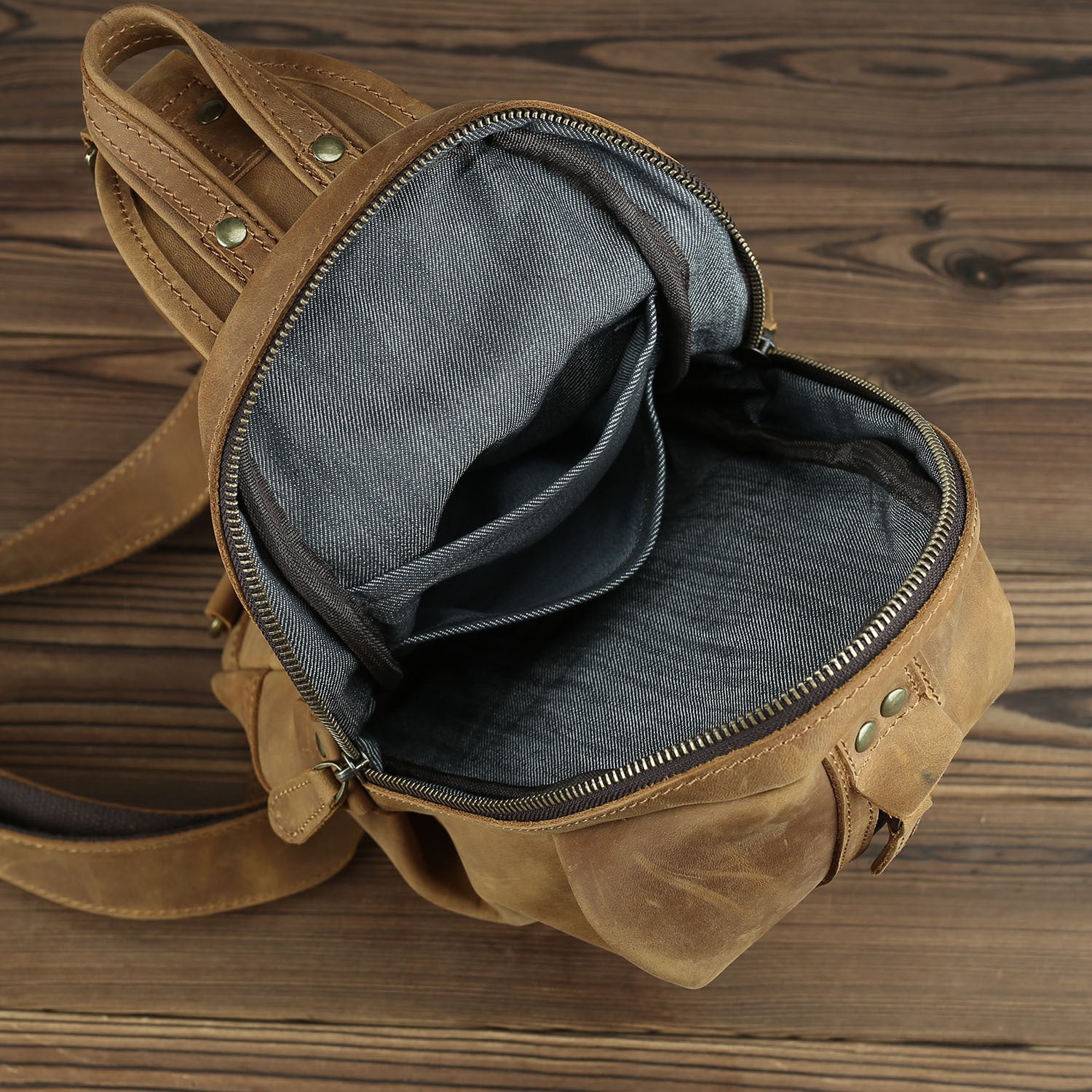 Rugged brown leather chest bag with ample interior storage on rustic wood background