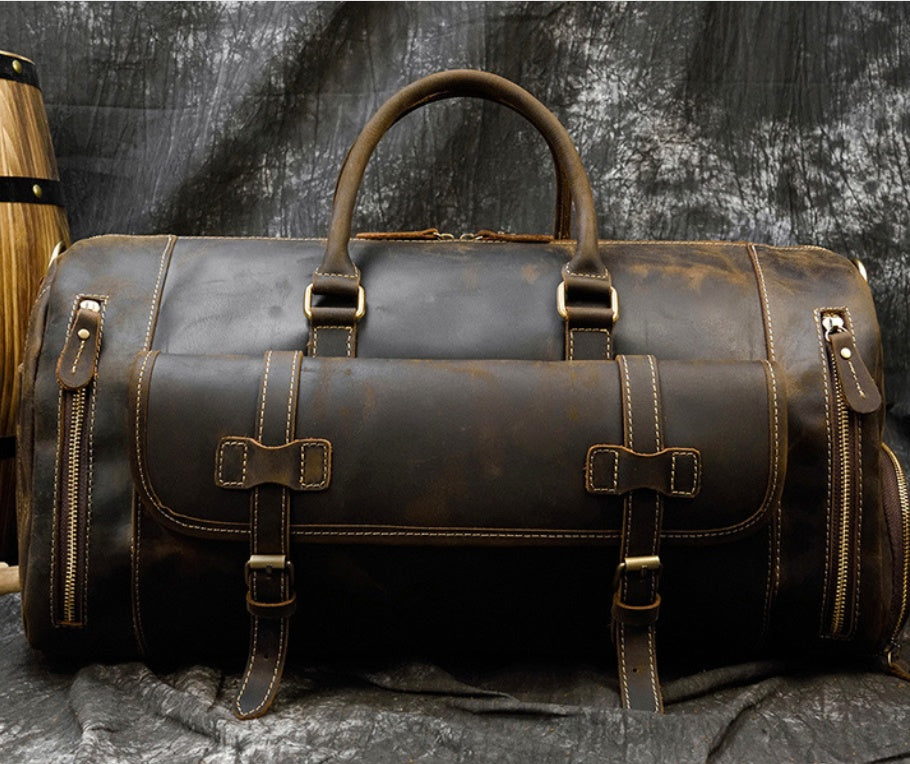 Vintage brown leather men's travel bag with multiple buckles, straps, and zippers displayed against a dark background.