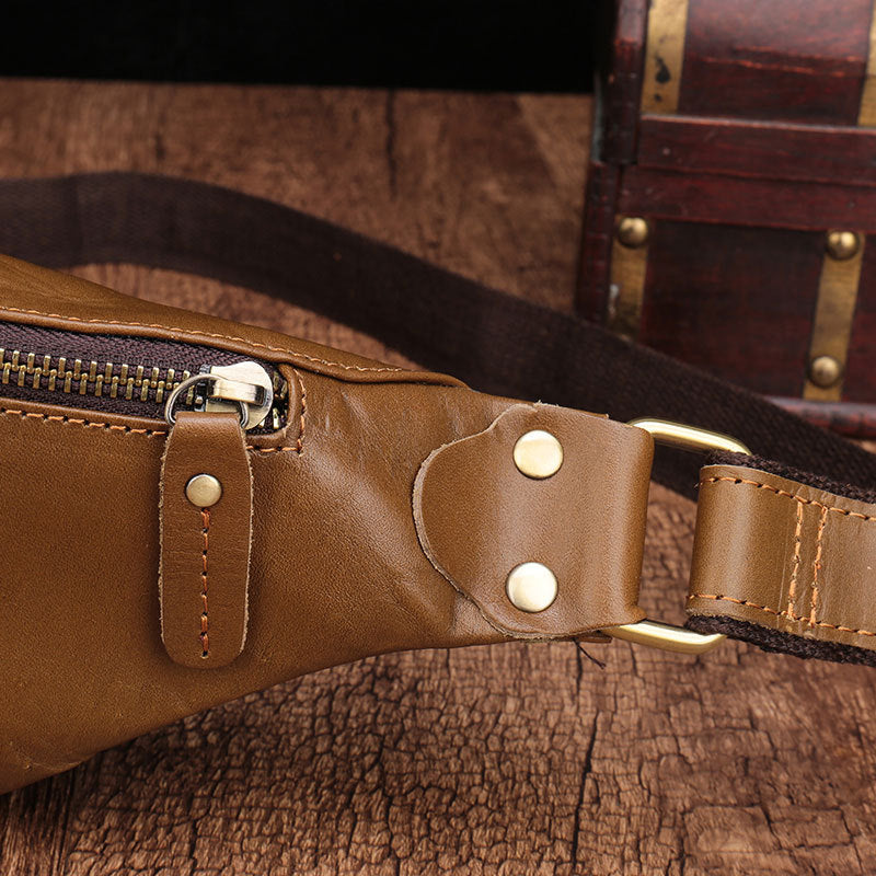 Leather men's cell phone belt bag with gold metal hardware and zippers, resting on a rustic wooden surface.