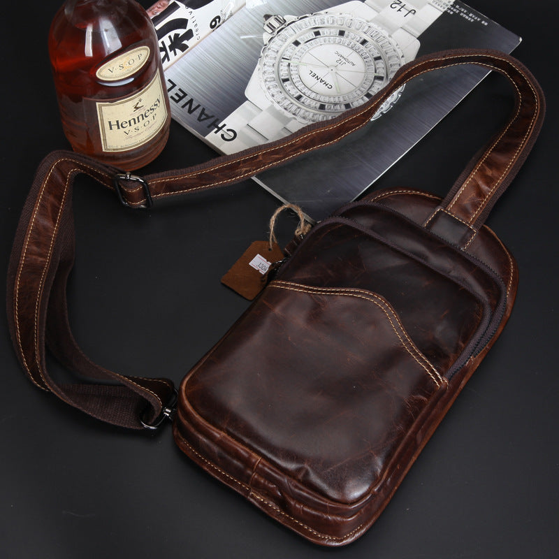 Vintage leather shoulder bag with retro accessories, including a bottle of Hennesy cognac and a classic analog compass, showcasing a sophisticated and stylish men's casual chest bag design.