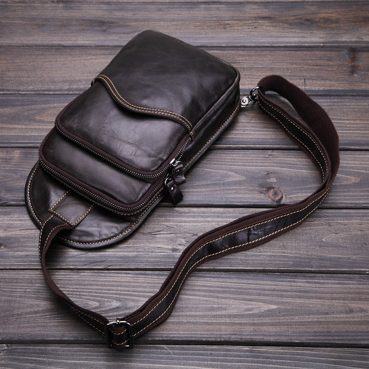 Sleek leather messenger bag with multiple compartments and adjustable strap on rustic wooden background.