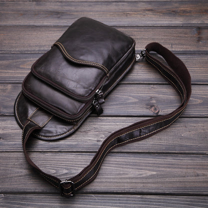 Sleek leather messenger bag with multiple compartments and adjustable strap on rustic wooden background.