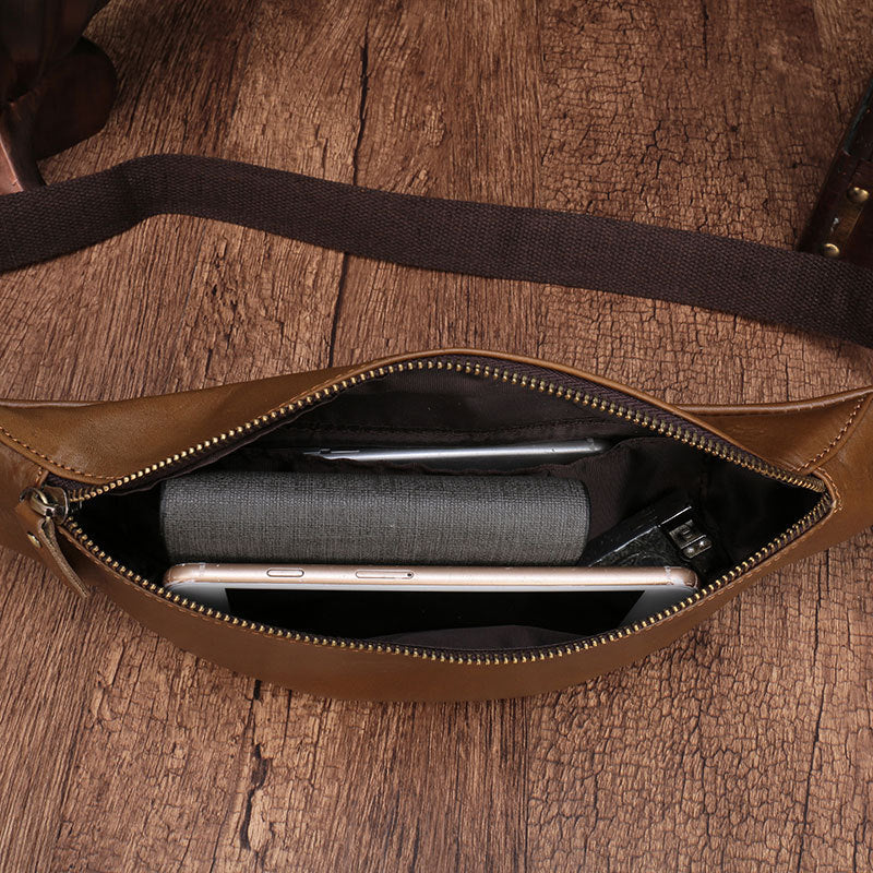 Leather men's cell phone belt bag with zipper compartment holding a mobile device on a wooden background.