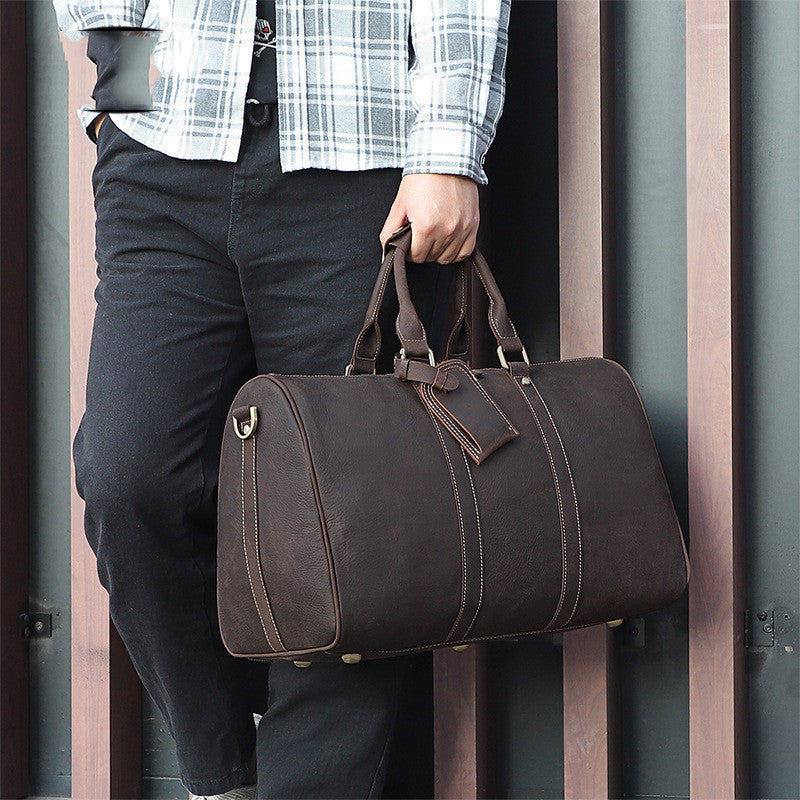 Vintage distressed men's leather travel luggage bag held by person wearing black pants and checked shirt