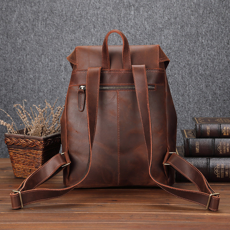 Stylish brown leather backpack featured on a wooden table next to a basket of twigs and books, showcasing its sleek and functional design for men's casual travel needs.